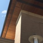 Modern building corner with wooden roof and brick wall under blue sky.